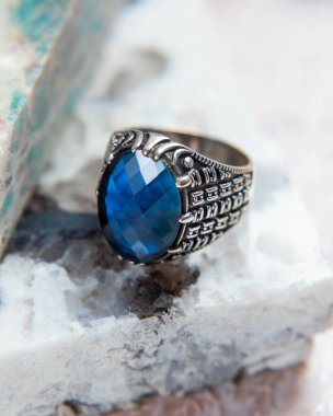 Beyaz mermer arka planda mavi mücevherli gümüş adam yüzüğü.