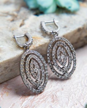 Bir çift oval elmas küpe ve taş bir yüzeyde Fransız kilidi var.