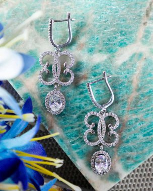 Çiçek desenli göz kamaştırıcı elmas küpeler yeşil mermer bir yüzeyde dinleniyor, zarafet ve lüks yayıyor.