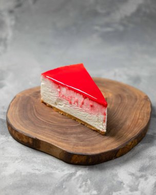 Kremalı cheesecake, kırmızı kaplamalı. Gri arka planda, ahşap bir tahtada oturuyor.