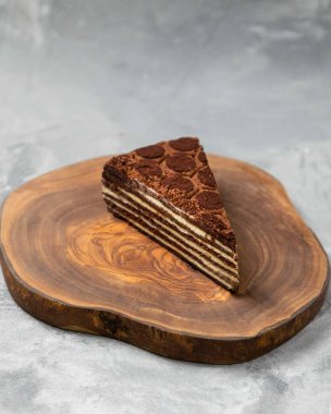 Üzerinde çikolata parçacıkları olan çok katmanlı çikolatalı pasta dilimi, tahta bir tahtanın üzerinde oturuyor.