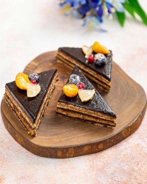 Çikolatalı pasta dilimleri, üzerinde çikolata ganache, physalis, yaban mersini ve limon dilimleri, ahşap tahtada yatıyor.