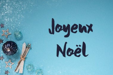 Fransız mesajlı kart Joyeux Noel Mutlu Noeller demek. Turkuaz ve Mavi Soğuk Noel arkaplanı Balo, Yıldız, Kayak ve Kar Taneleri gibi süslerle süslenmiş.
