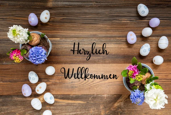 复活节平躺着德语文本Herzlich Willkommen的意思是欢迎 有复活节彩蛋装饰和装饰品的花朵 具有木制 古色古香背景的百合花排列 — 图库照片