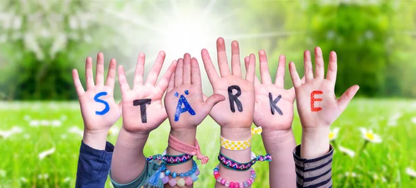 孩子们手握多彩的德语单词Staerke意味着力量 阳光碧绿的草场作为背景 — 图库照片