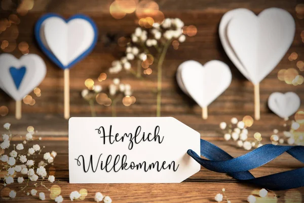 ドイツ語のテキスト ヘルツリヒとラベル ウィルザーニャは歓迎します ハート 青い弓のような白いお祝いと大気の装飾 ヴィンテージ スパークリングライト付きの木製の背景 — ストック写真