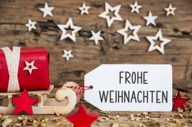 Kırmızı hediyeli ahşap kızak ve Almanca yazılı etiketli kırsal Noel arkaplanı Frohe Weihnachten, bu da İngilizce 'de mutlu noeller demek.