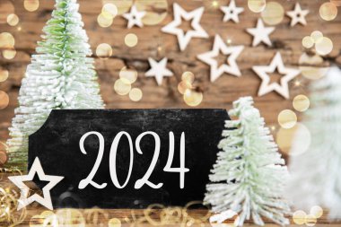 Ahşap arka planı olan yeşil beyaz Noel ağaçları ve 2024 nolu metni olan siyah bir işaret.