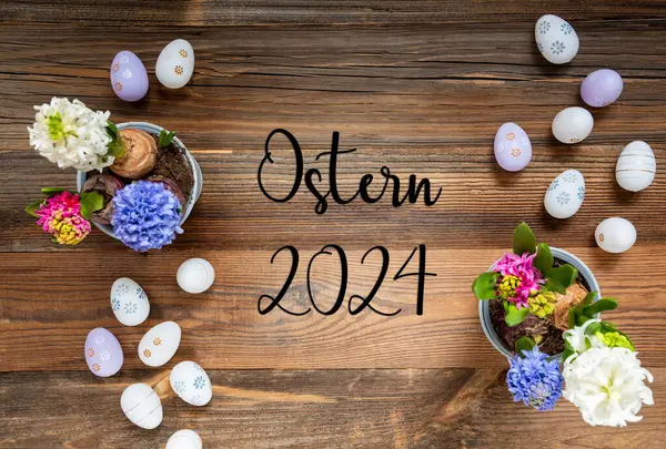 复活节平铺与德语文本Ostern 2024意味着复活节2024 有复活节彩蛋装饰和装饰品的花朵 具有木制 古色古香背景的百合花排列 免版税图库照片