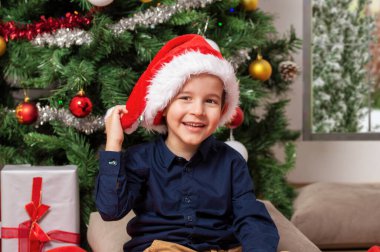 Küçük çocuk Noel hediye kutularıyla süslü bir Noel ağacının yanında oturuyor. Evinde mutlu bir beyaz çocuk oturuyor.