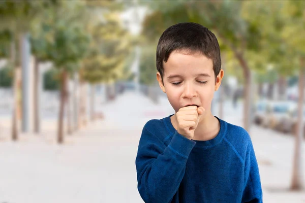 青いシャツを着て街を歩く子供は気分が悪くなり 風邪や気管支炎の症状として咳をします ヘルスケアの概念 — ストック写真