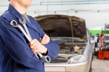 Cropped image of a male mechanic standing while holding two wrenches in a car mechanic shop
