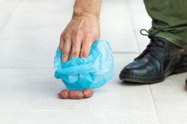 Closeup of the hand of a man picking up some dog poop with a bag clipart