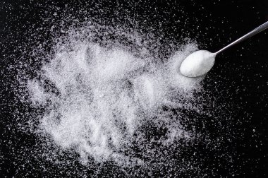 Spoon with white sugar on the dark background and copy space