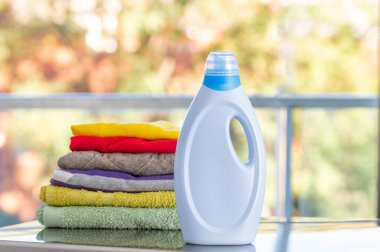 Bir şişe deterjan ve çamaşır makinesinin tepesinde bir yığın çamaşır.
