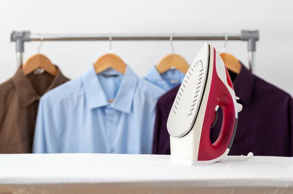 Electric iron and pile of clothes on ironing board at home with copy space.