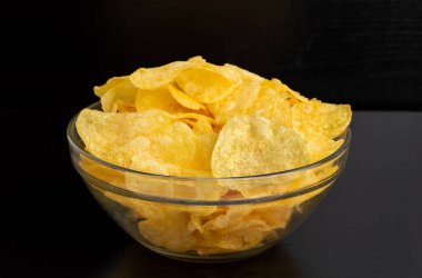 Crispy potato chips in white bowl with black background