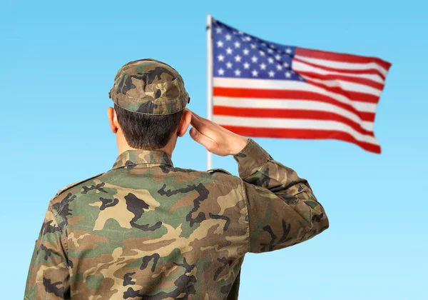 Rear view of a young soldier standing to a the US flag and saluting