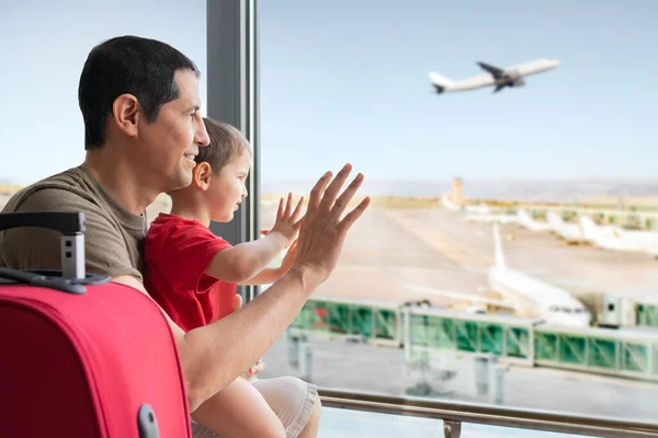 Rear view of a family looking and waving through the window to a plane in an airport