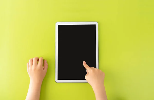 High angle shot of a little kid using a digital tablet with tablet computer on green background in vertical with copy space.