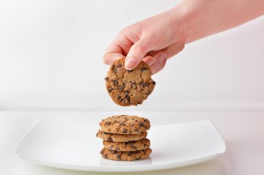 Woman holding by her hand a chocolate cookie from a white pl