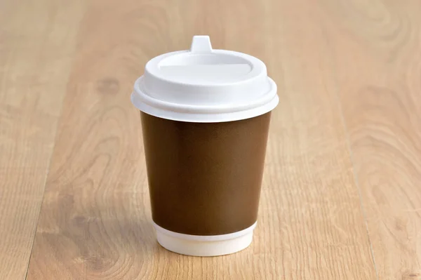 Disposable paper cup of coffee on wooden table
