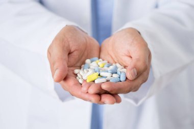 Elinde çeşitli haplar tutan kimliği belirsiz bir erkek doktorun yakın plan fotoğrafı.