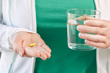 Shot of an unrecognizable young  woman hand showing a capsule and a glass of water 