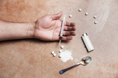 Bir uyuşturucu bağımlısının yakın plan çekimi. Yanında uyuşturucu teçhizatı yatarken kolu gevşektir. 