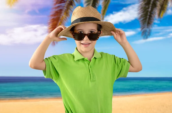 ビーチで緑のTシャツの帽子のサングラスをかけて休暇中の子供は笑顔でカメラを見ています 正の人 — ストック写真