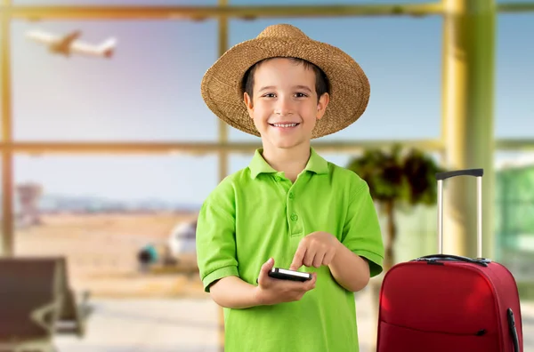 在机场 白人小男孩用智能手机看着镜头 满脸喜色 头戴一顶帽子 自信地微笑着 露出牙齿 — 图库照片