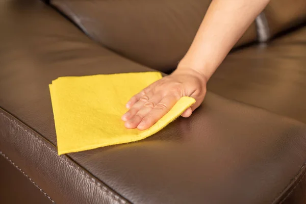 一个女人在家里用黄色抹布擦黑色皮沙发时被枪击中 — 图库照片