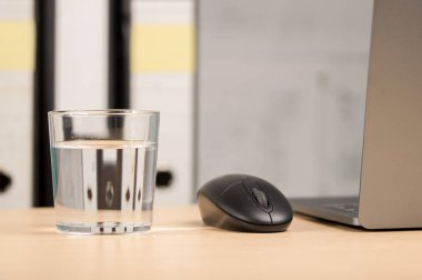 Ofiste dizüstü bilgisayarı ve bir bardak su olan bir fareyi yakın plan çek.