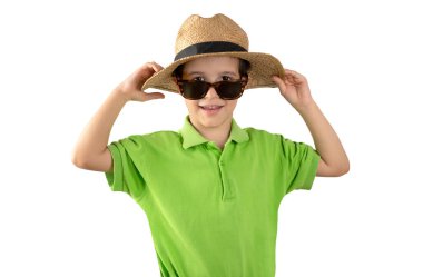 Yeşil t-shirt şapkalı ve güneş gözlüklü bir çocuk beyaz arka planda şapkayı kaldırıyor. Mutlu yüzlü çocuk gülümseyip kameraya bakıyor. Pozitif kişi