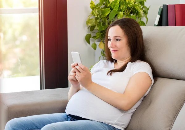 妊娠中の女性が自宅で携帯電話のコンテンツをチェックするショット — ストック写真