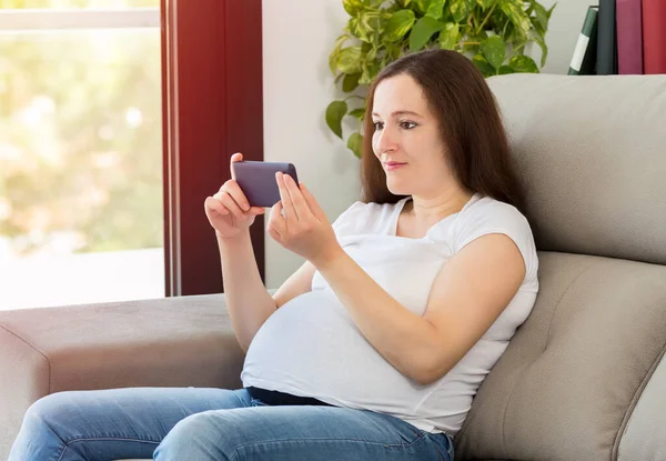 自宅の携帯電話でメディアコンテンツを見て妊娠中の女性のショット — ストック写真