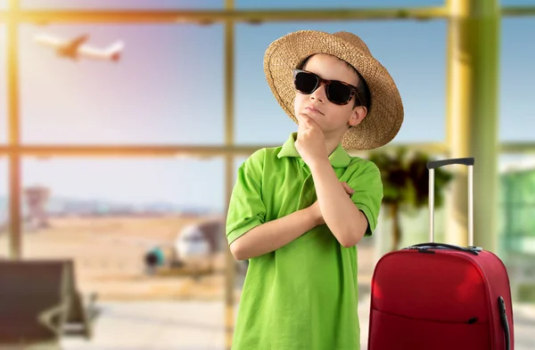 休暇中の男の子の質問について考えてあごの手で空港で緑のTシャツの帽子をかぶってサングラスをかけて 包括的な表現 ペナルティ フェイス 疑いの概念と脇を見る — ストック写真