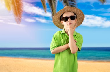 Sahilde yeşil tişörtlü güneş gözlüğü takan, gülümseyen ve kameraya bakan bir çocuk. Pozitif kişi