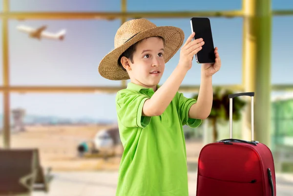 在机场 白人小男孩一边笑着一边用智能手机自拍 — 图库照片