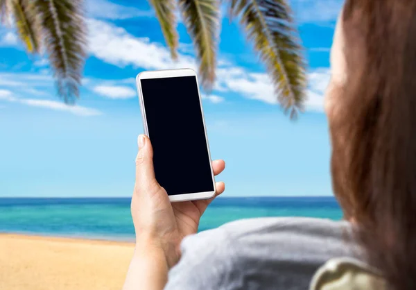 女人坐在海滩的沙发上 观看着一个空白的智能手机屏幕 — 图库照片