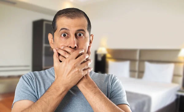 Shocked man covering his mouth with hands at hotel