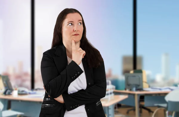 オフィスに立ってスーツを着て美しいビジネス女性 あごに指で疑いに集中し 疑問を見上げ考える — ストック写真