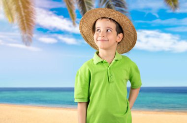Plajda yeşil tişört ve şapka giyen küçük çocuk soru sormayı ve düşünceli ifadeyi düşünüyor. Düşünceli bir yüzle gülümsüyor. Şüphe kavramı.