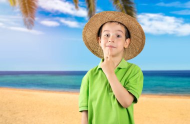 Kumsalda yeşil t-shirt ve şapka giyen, eli çenesinde soru soran, düşünceli bir çocuk. Düşünceli bir yüzle gülümsüyor. Şüphe kavramı.