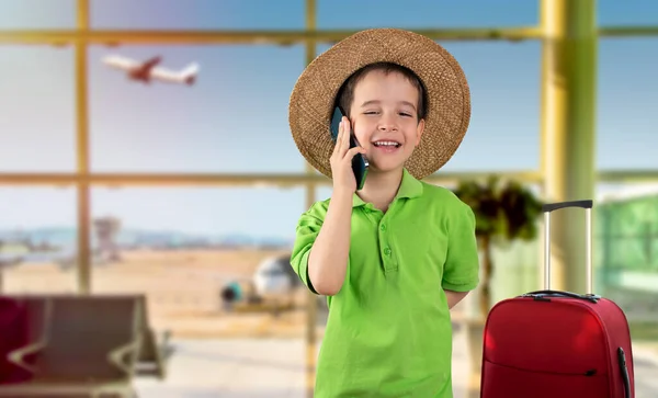 在机场 小男孩用智能手机 满脸喜笑 头戴礼帽 自信地笑着 露出牙齿 — 图库照片