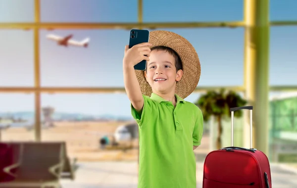 帽子をかぶった白人の小さな男の子と笑顔作りますセルフィーによってスマートフォンで国際空港 — ストック写真