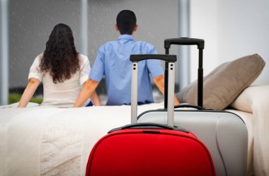 Arka planda, bir çift turistin ön planda bavullarıyla bir otel odasının penceresinden bakması.