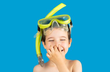 Tuba maskeli ve eli burnunda şnorkel olan çocuk gülümsüyor ve mutlu. Mutluluk kavramı. Şnorkelleme, yüzme, tatil konsepti mavi arka planda izole edildi.