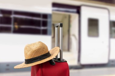 Seyahat ve tatil amacıyla tren istasyonunda saman şapkalı kırmızı renkli basit bir valiz..