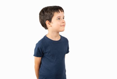 Beyaz arka plan üzerinde sıradan bir tişört giyen çocuk yüzünde gülümseme, doğal bir ifade ile bir o yana bir bu yana bakıyor. Kendinden emin gülen.